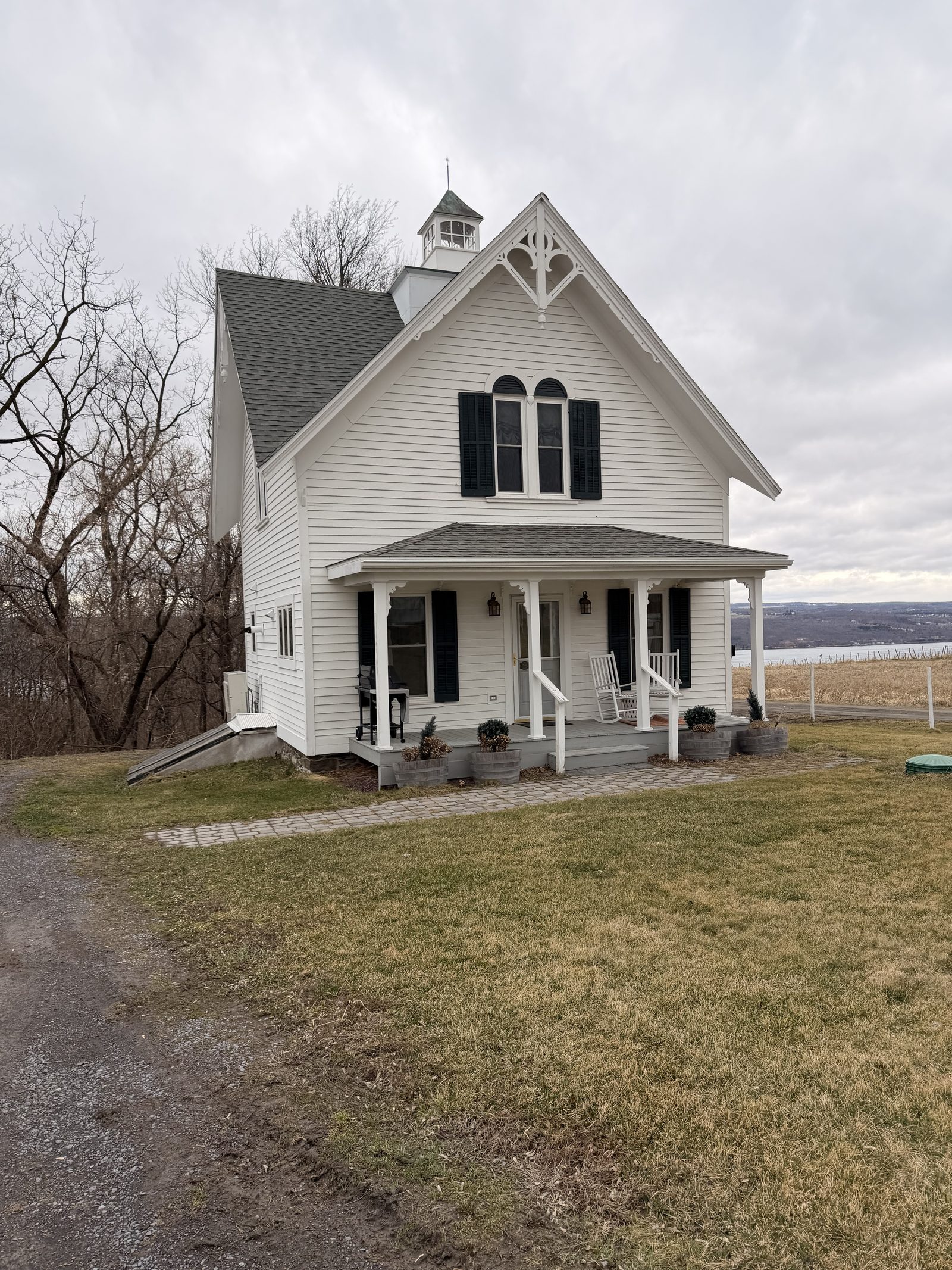 The white Victorian Fruit Packing House with cupola and covered porch, vineyard and Seneca Lake behind it