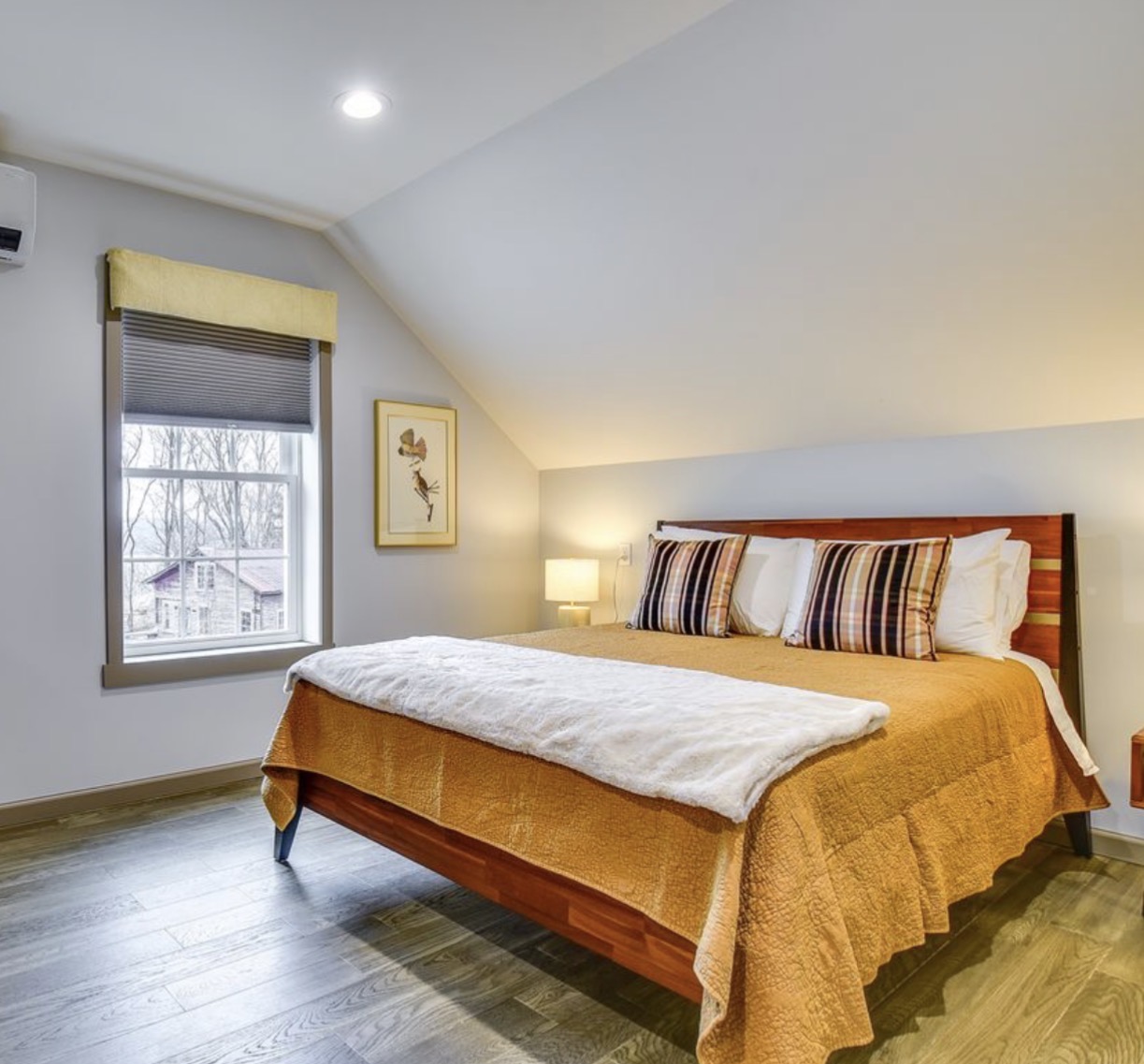 Upstairs bedroom with queen bed under the sloped roofline, window and wall-mounted mini-split