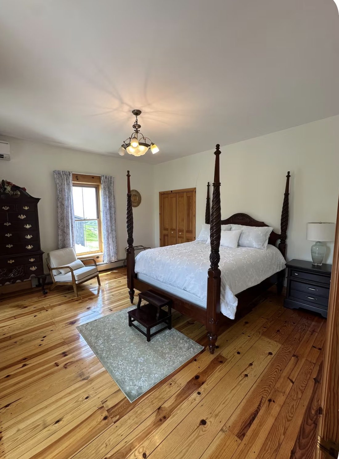 A bedroom with a carved dark-wood four-poster bed, antique highboy dresser, and wide-plank pine floors