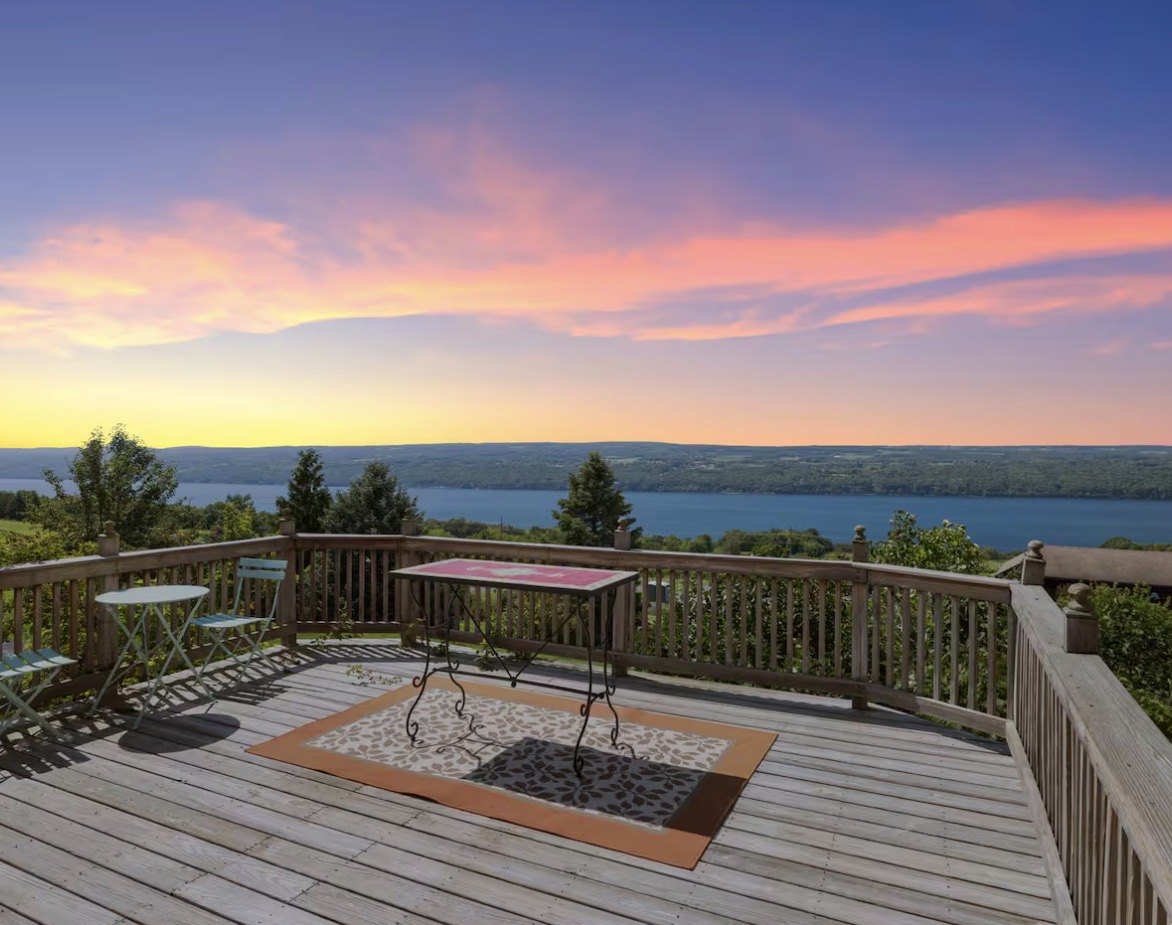The wrap-around deck of the French-inspired brick farmhouse at sunset, with a bistro set overlooking Seneca Lake