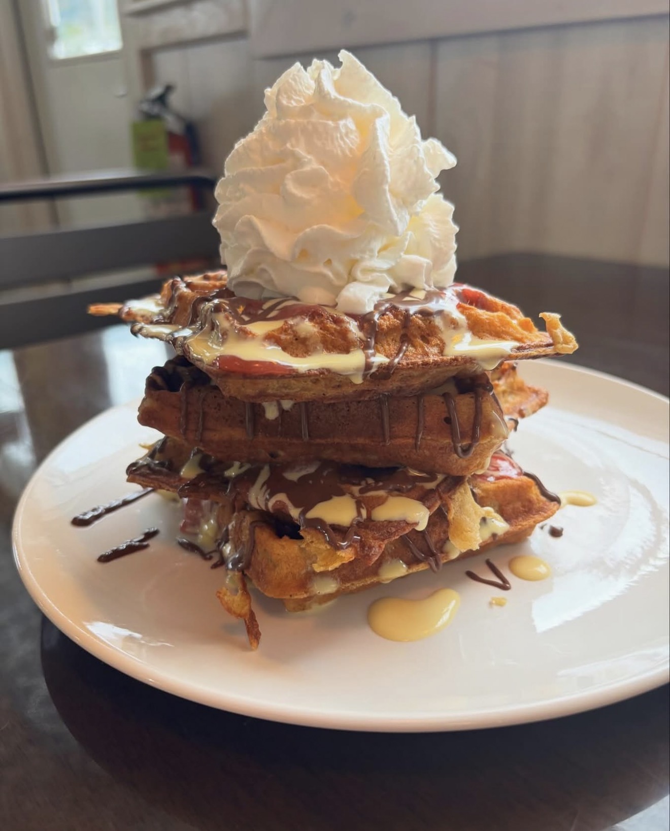 A tall stack of waffles at Johnny's Kitchen, layered with sauces and topped with whipped cream