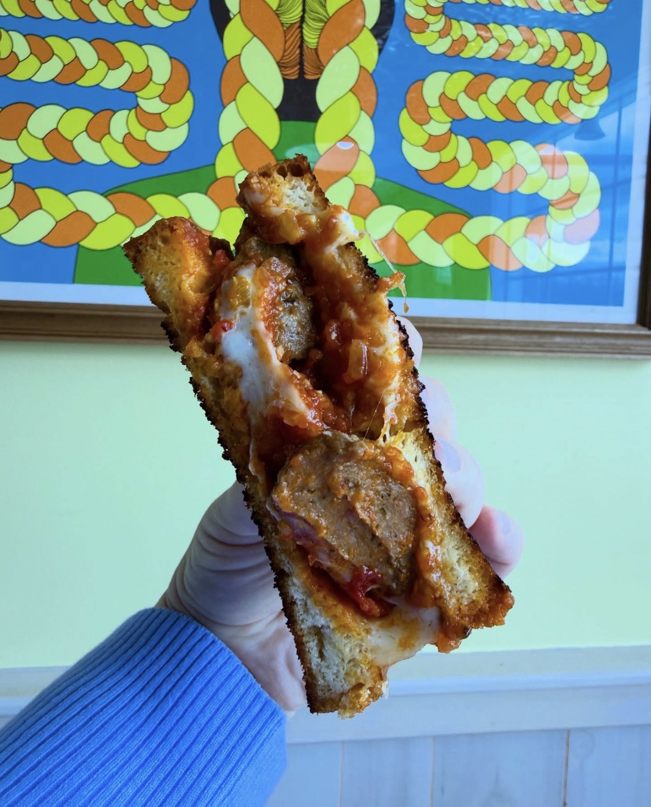 A meatball and melted mozzarella sandwich on griddled house bread, held up in the dining room