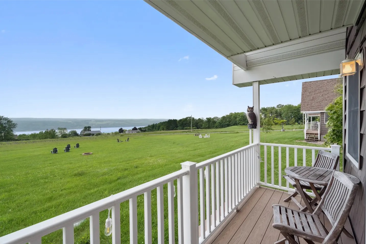 Covered villa porch with chairs looking out over the lawn, fire pit circle, and Seneca Lake beyond