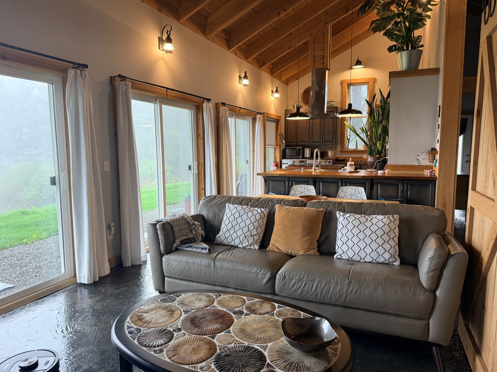 EcoBarn great room with vaulted timber-frame ceiling, leather sofa, glass doors to the lawn, and sliding barn door
