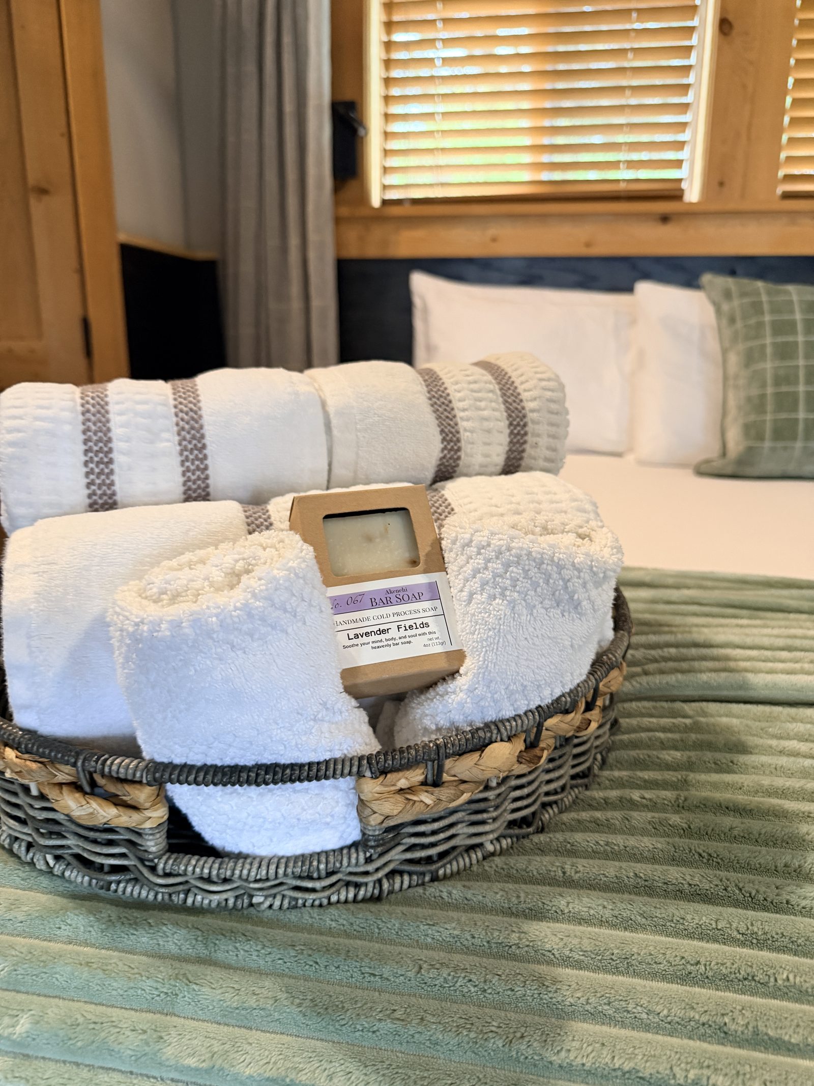 Basket of rolled towels with a handmade lavender bar soap set out on the bed